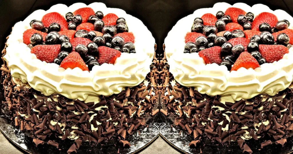 Bolo de chocolate com raspas de chocolate nas bordas com chantily e morangos por cima