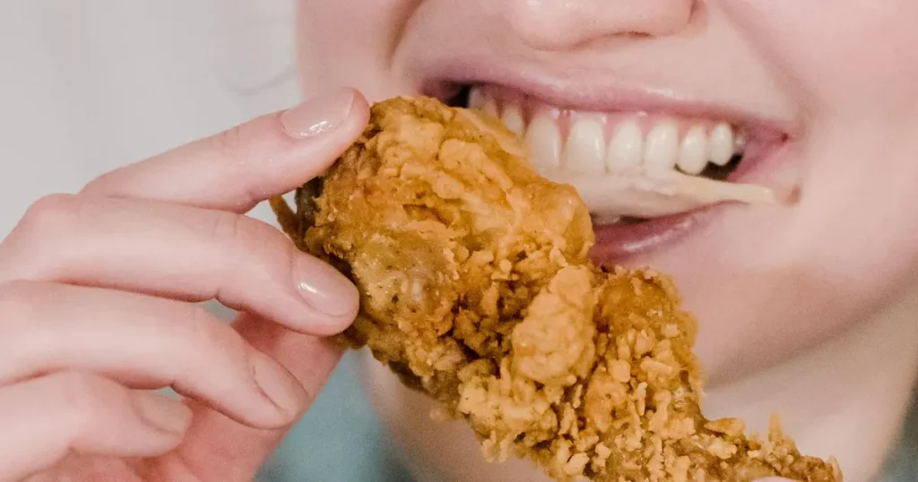 mulher mordendo em um pedaço de frango frito no ponto certo